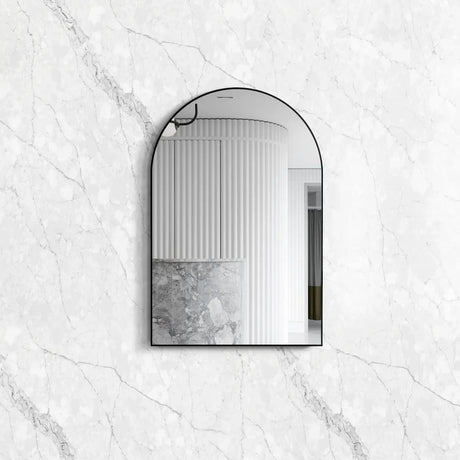Archie 900x600 Black Metal Framed Mirror with an elegant arched design, reflecting a modern interior against a polished white marble-textured background.