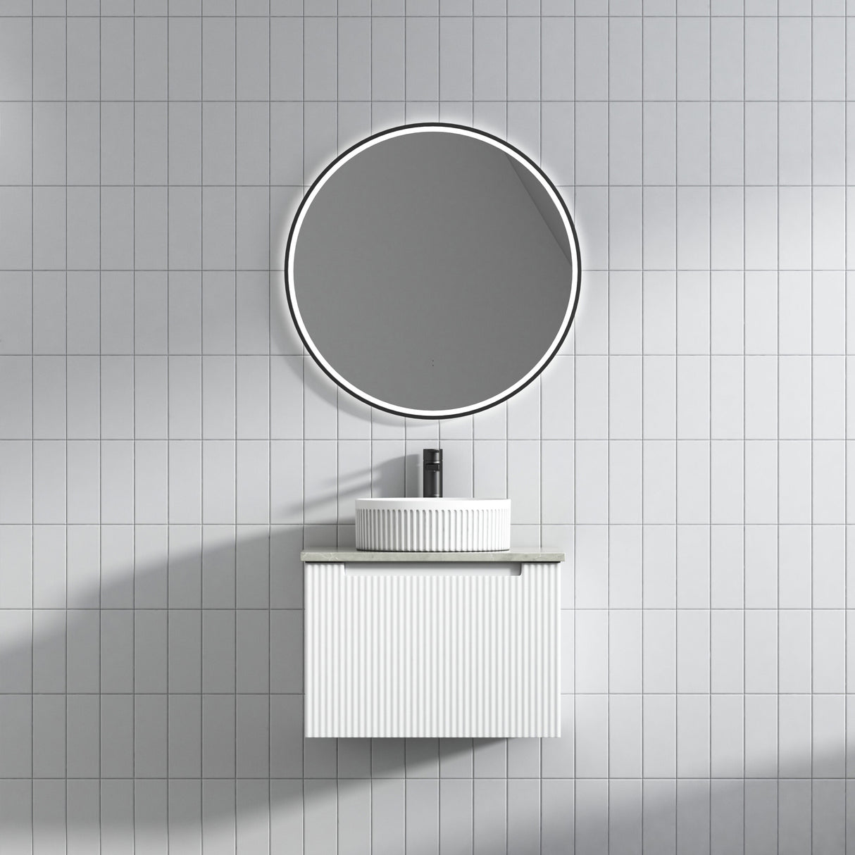 Bathroom setup with round mirror and white vanity against a tiled wall.