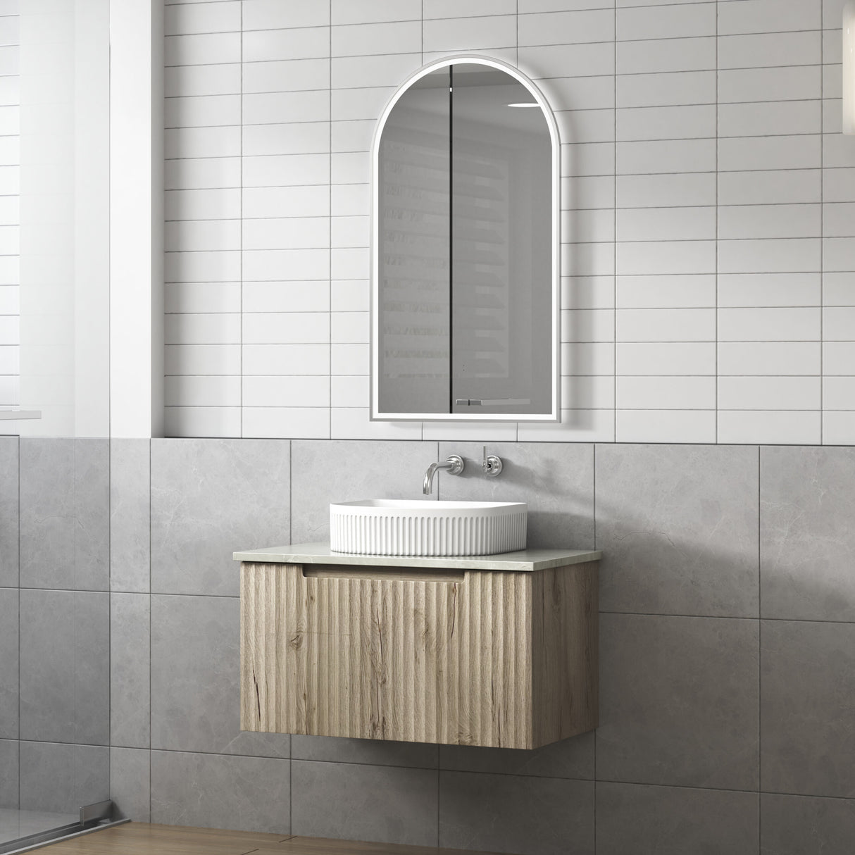 Bathroom with wooden vanity, white sink, and arched mirror on gray tiled wall