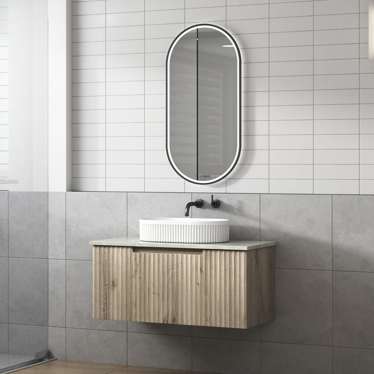 Bathroom with wooden vanity, white sink, and oval mirror on tiled wall