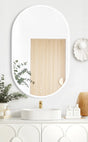 LED Noosa Mirror in 900x600 dimensions with a white metal frame, mounted above a modern white vanity, accented by a round vessel sink, gold faucet, and natural décor elements including eucalyptus and wicker.