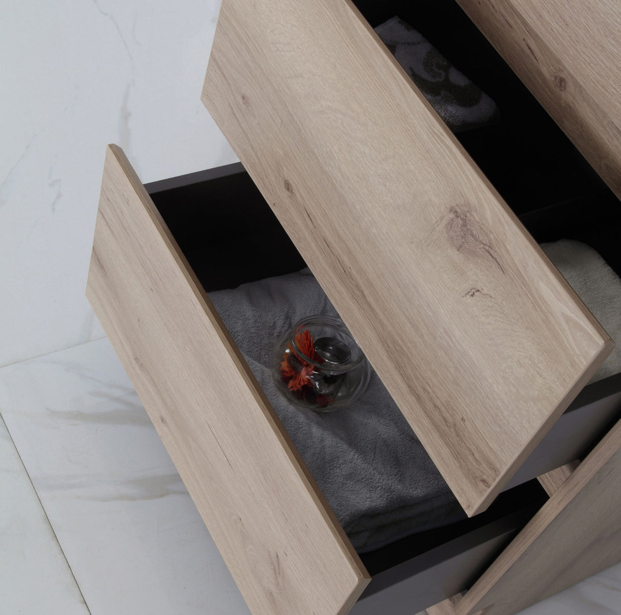 Wooden drawer with a glass containing red flowers on a white floor.