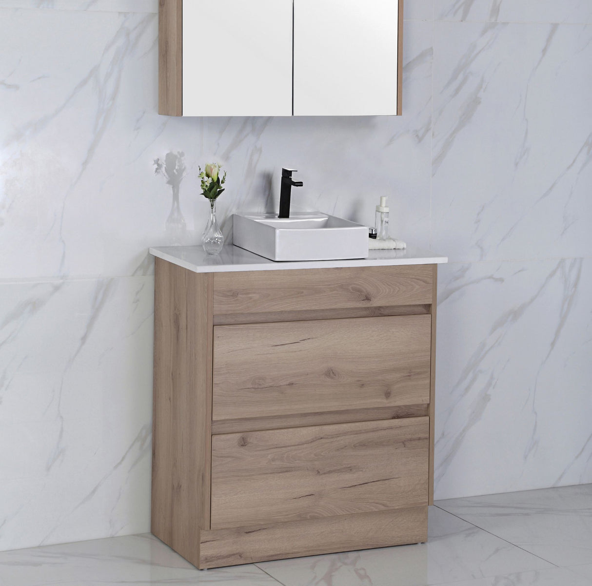 Bathroom vanity with wooden cabinet and white countertop against a marble wall.