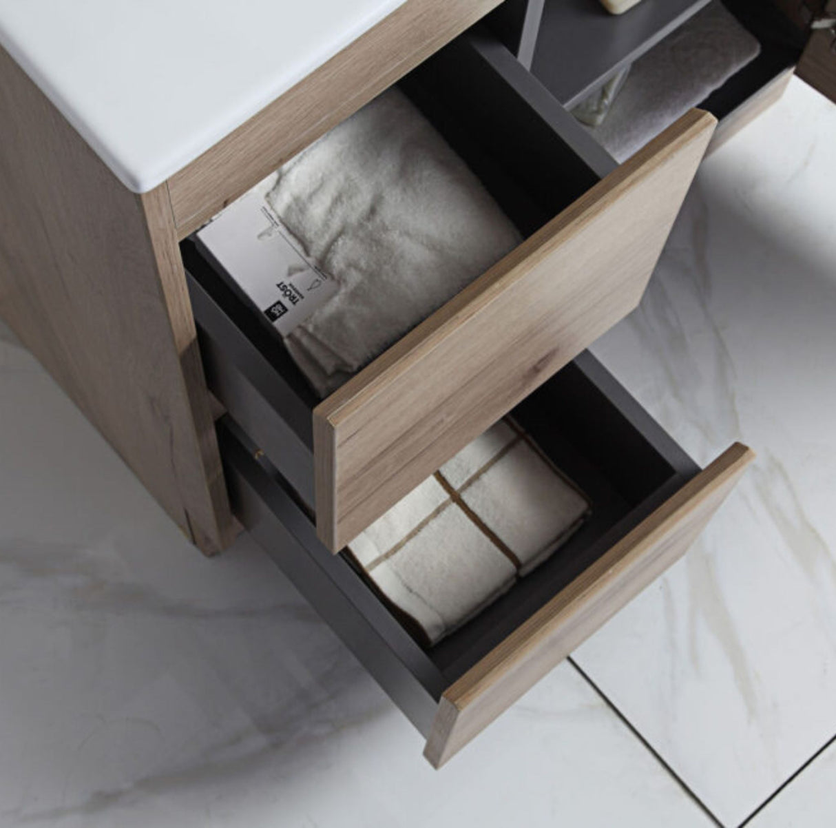 Bathroom vanity with open drawer containing towels on a tiled floor.