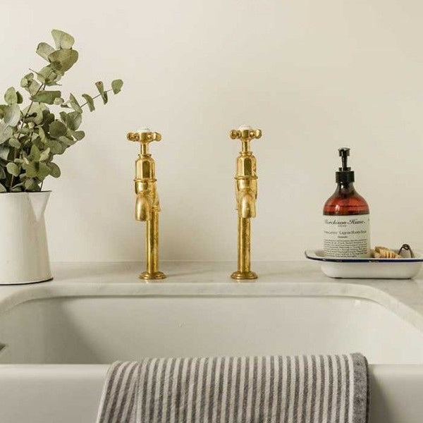 Bathroom sink with gold fixtures, a vase of greenery, and a soap dispenser.