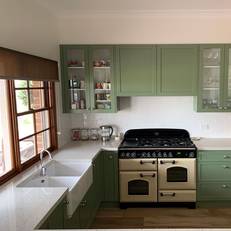 Modern kitchen with green cabinets, white countertops, and a brick wall.
