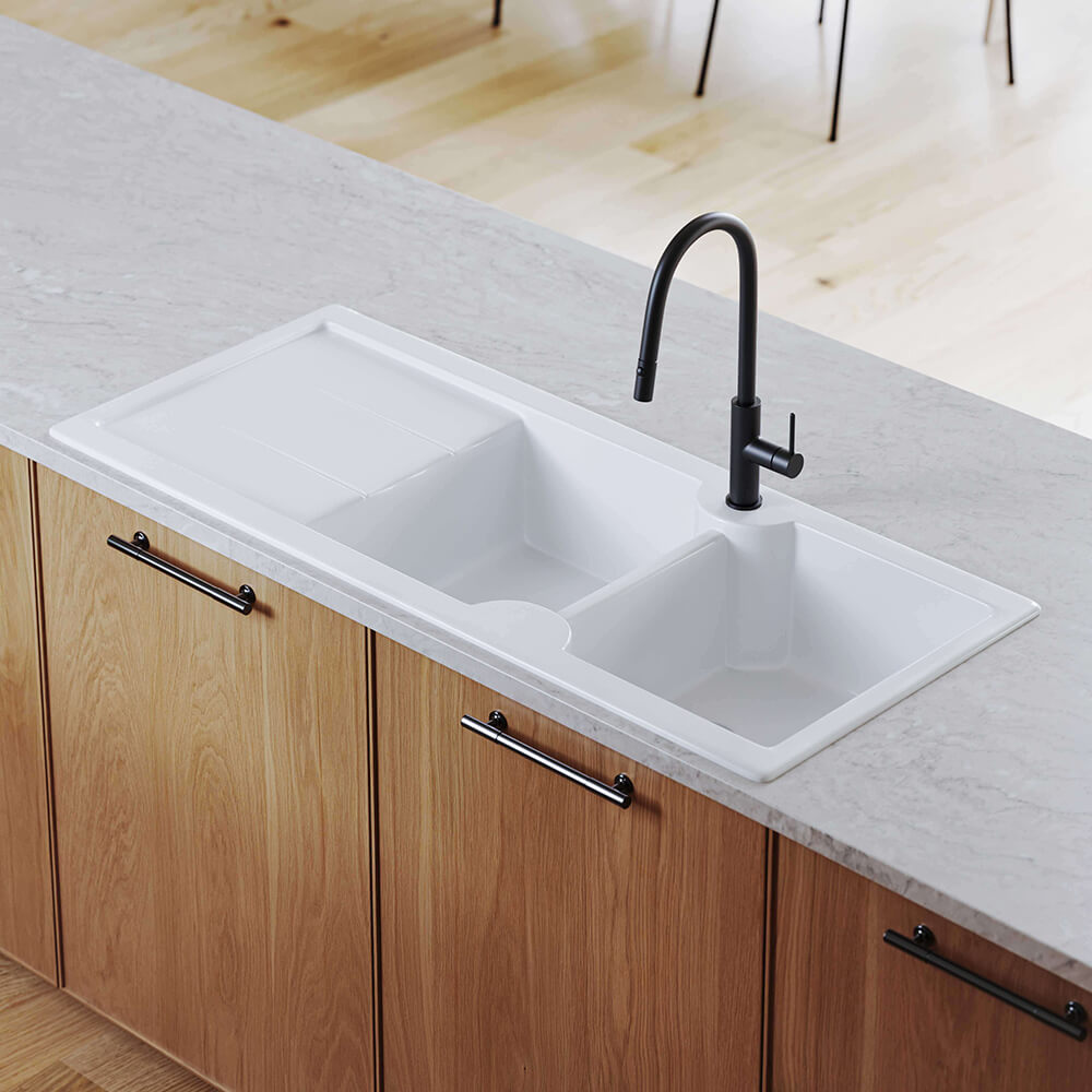 White kitchen sink with black faucet on a countertop with wooden cabinets.