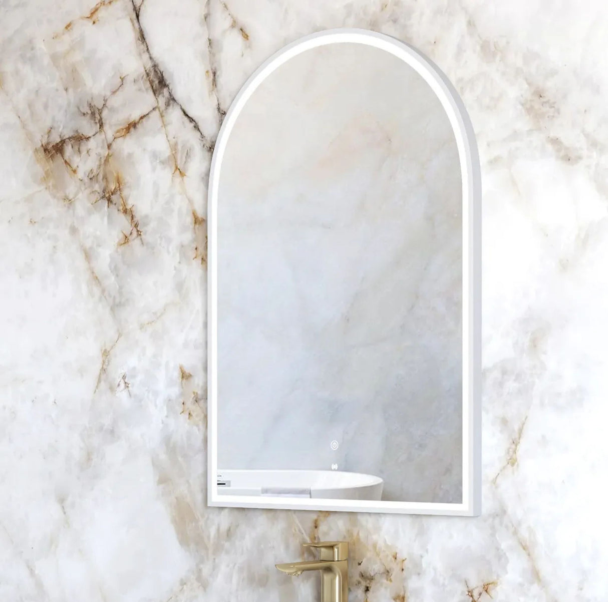 Arch-shaped mirror on a marble wall with a gold faucet.