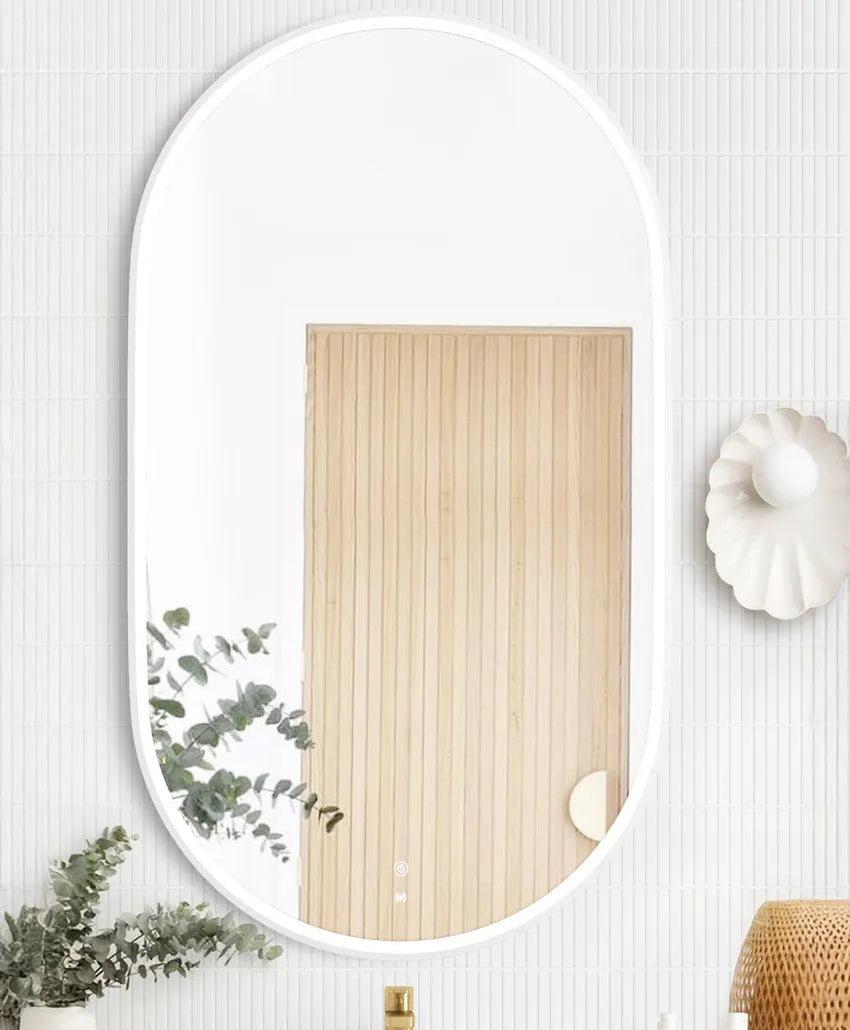 LED Noosa mirror (1200x750) with a sleek white metal frame, mounted above a modern white vanity. The bathroom setup includes a round basin, gold faucet, eucalyptus in a decorative vase, and al.ive hand soap bottles, creating a minimalist and elegant aesthetic.