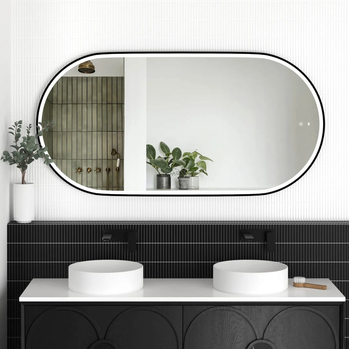 LED Noosa mirror (1500x750) with a sleek black metal frame, mounted above a modern black vanity featuring arched detailing. The bathroom setup includes dual round basins, matte black faucets, and greenery accents, creating a striking monochromatic design.