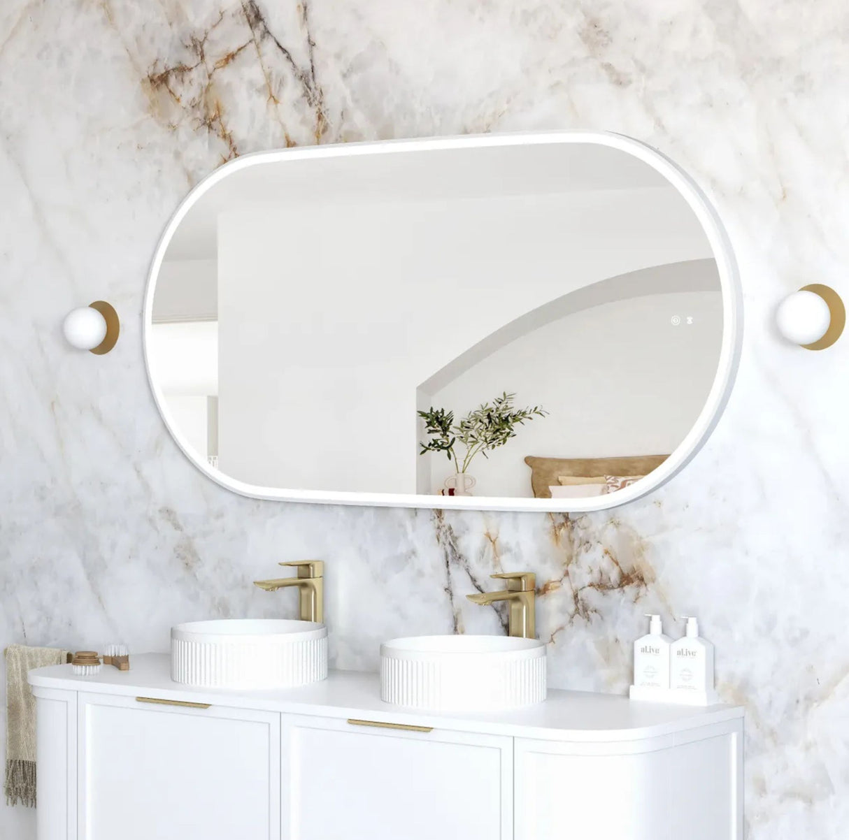 Bathroom vanity with white sinks, gold fixtures, and a large mirror on a marble wall.