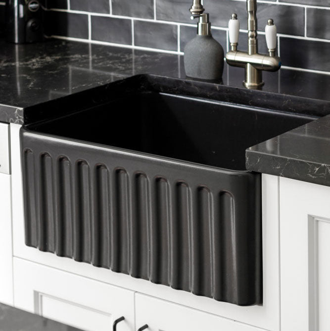 Black farmhouse sink in a kitchen with dark tiled wall and countertop.