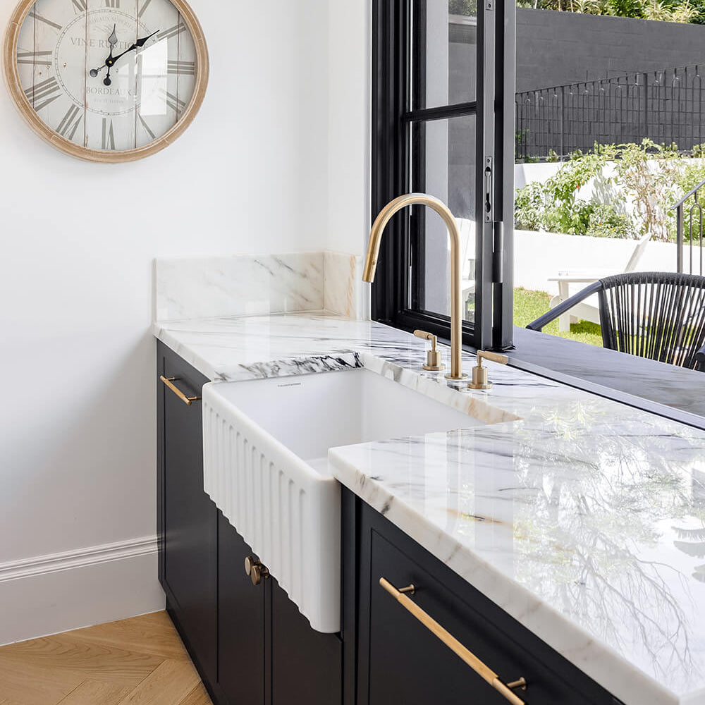 Modern kitchen with black cabinets, white marble countertop, and a clock on the wall.
