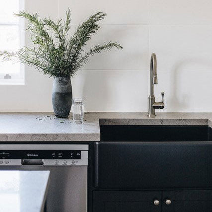 Modern kitchen with black sink, white cabinets, and a vase of greenery on the counter.