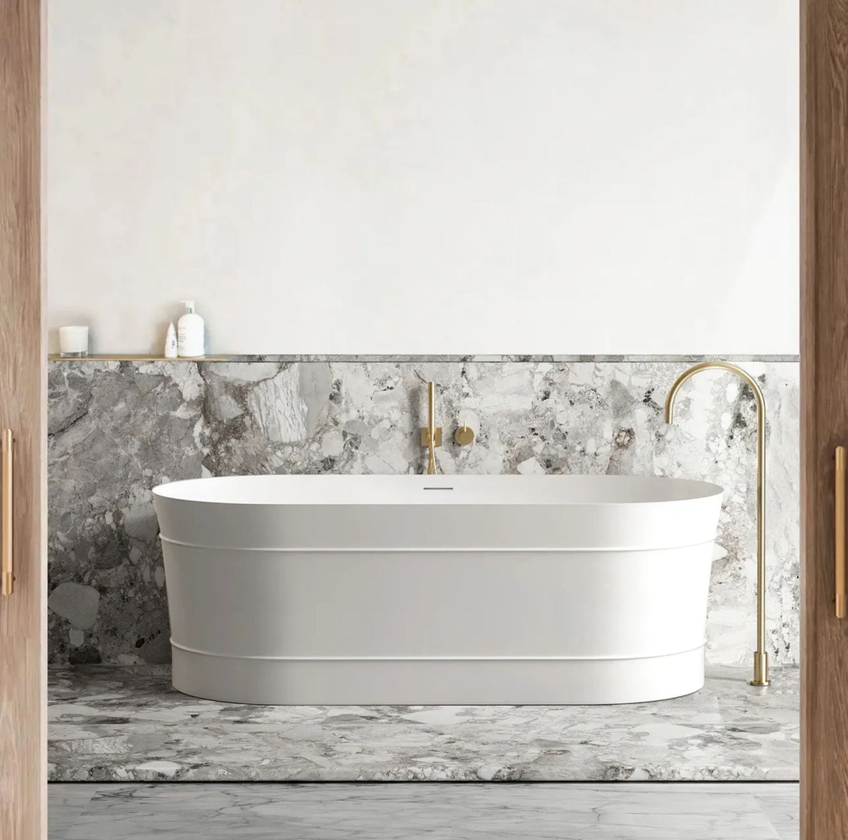 White freestanding bathtub in a bathroom with marble walls and gold fixtures.