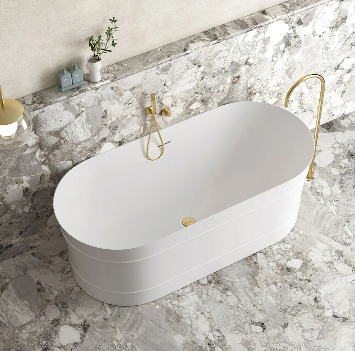 White freestanding bathtub with gold fixtures in a marble bathroom.