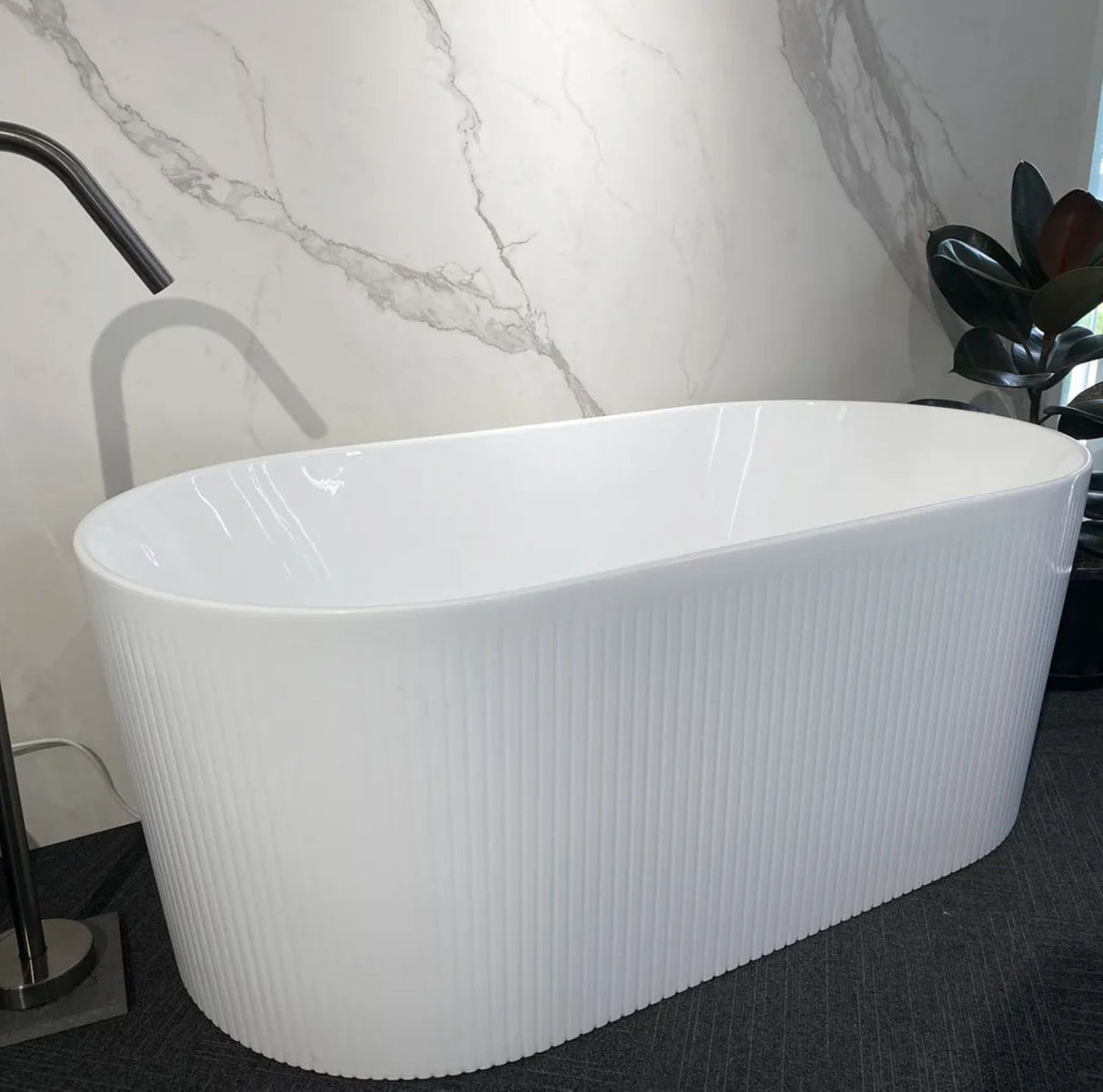 White freestanding bathtub in a bathroom setting with marble wall and plant.