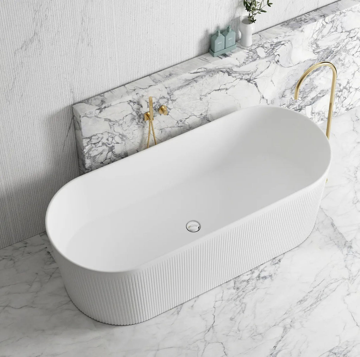 White freestanding bathtub with gold fixtures on a marble bathroom floor.