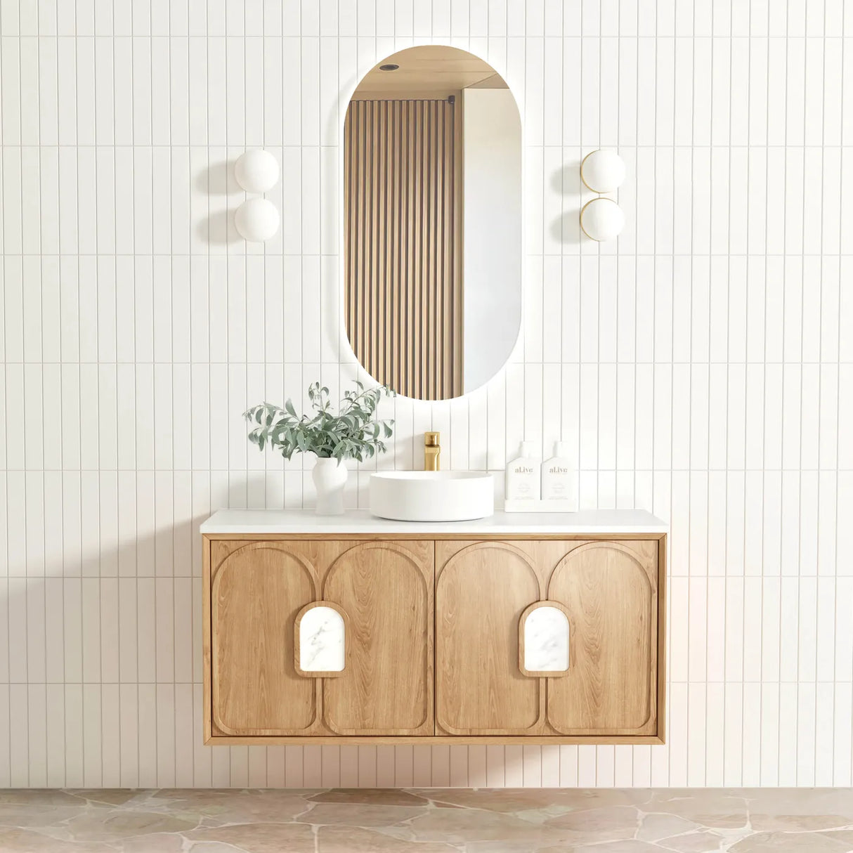 Bathroom vanity with wooden cabinet, round mirror, and decorative plant against a light tiled wall.