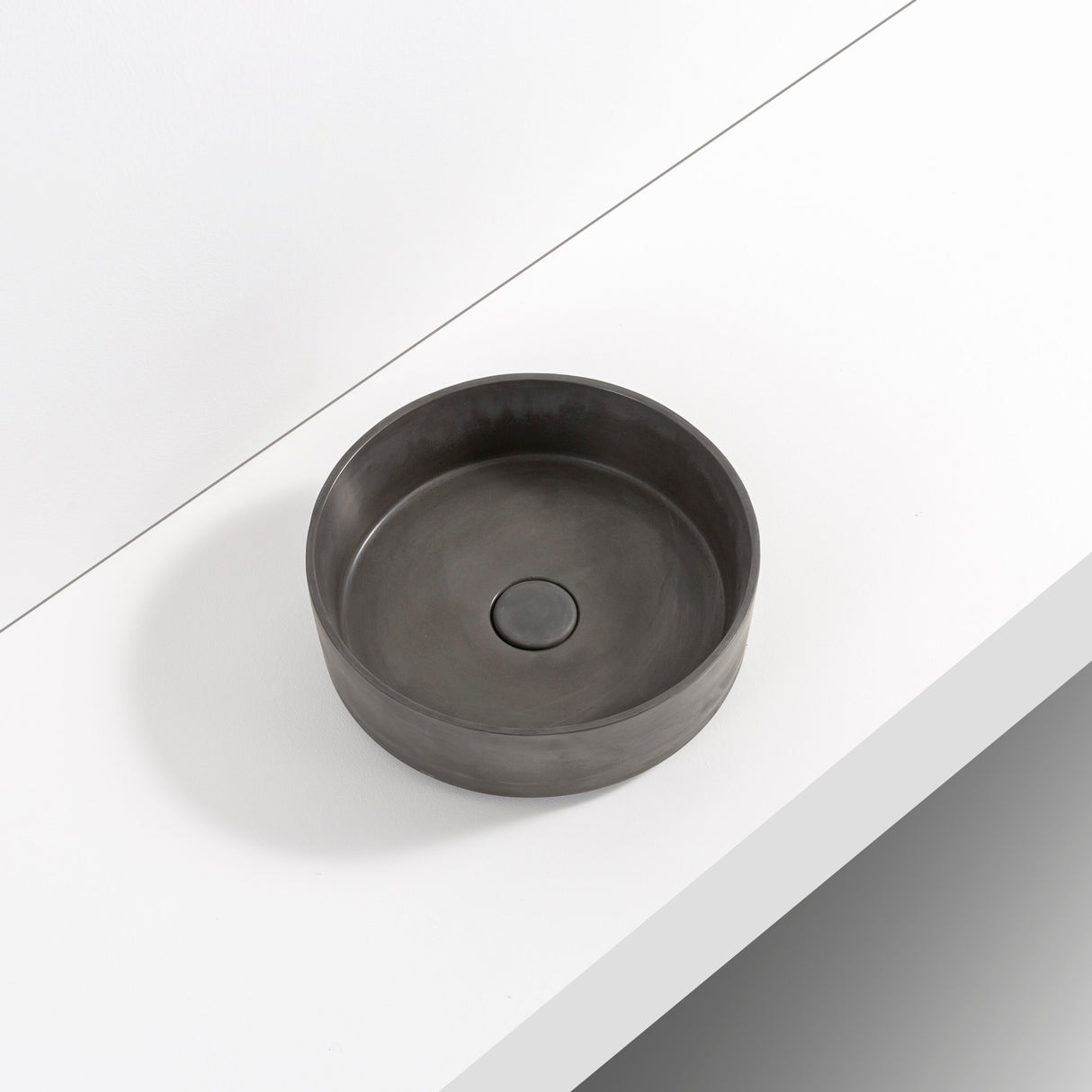 ARLO Round Concrete Basin in Charcoal, featuring a smooth matte interior with an integrated circular drain, elegantly displayed on a minimalist white surface.