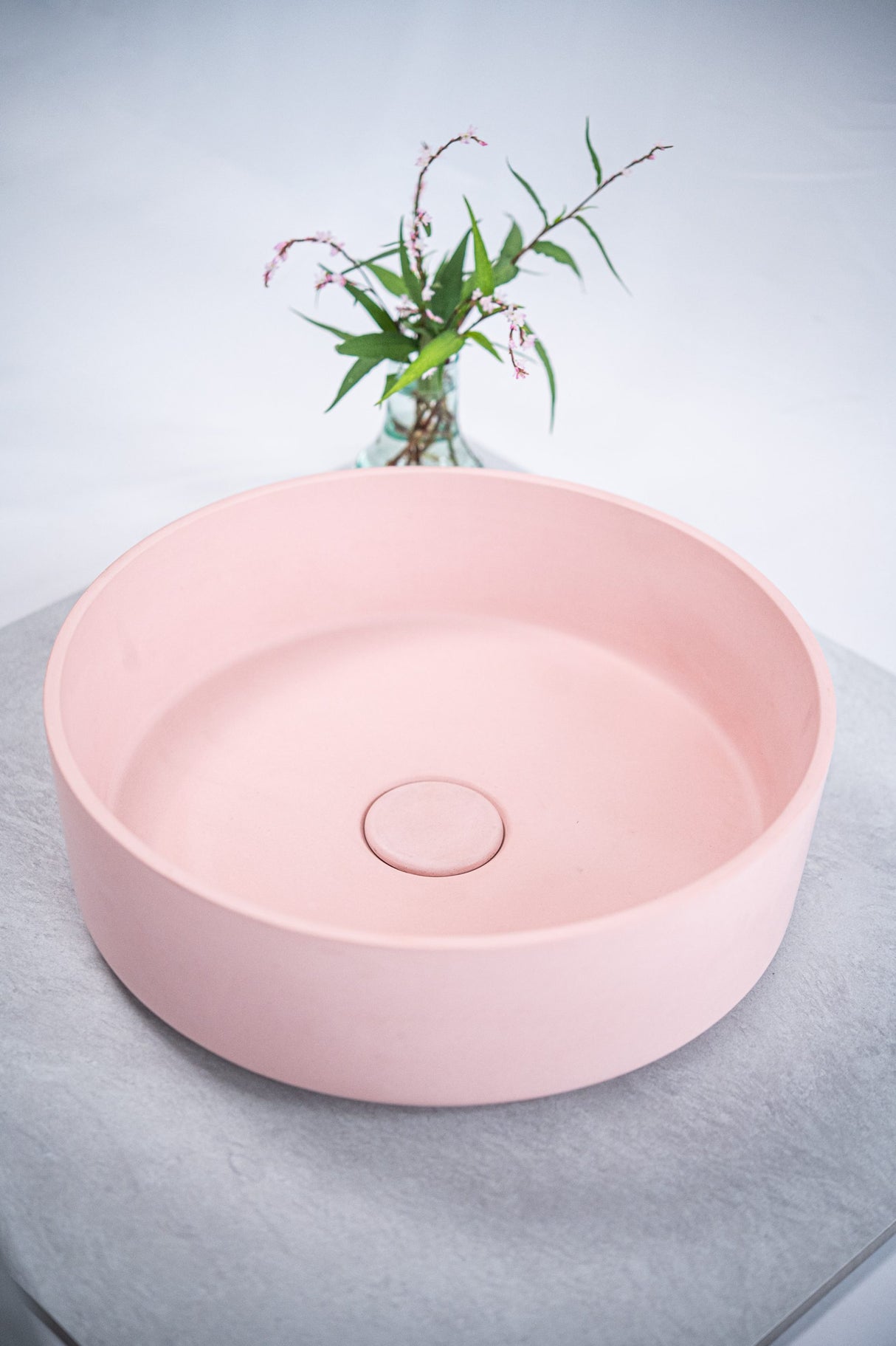 ARLO Round Concrete Basin in Dusty Pink, featuring a smooth matte finish and minimalist design, complemented by a vase of delicate greenery for a soft and modern bathroom aesthetic.