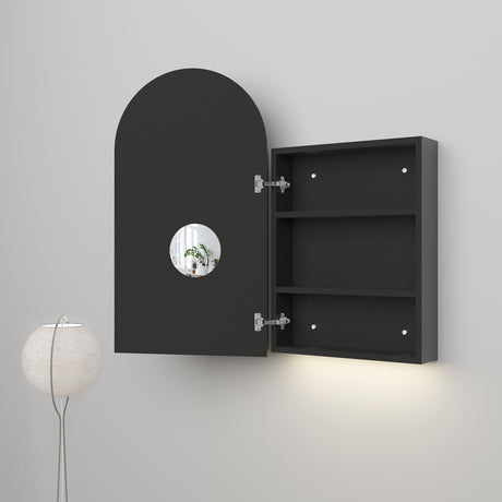 Modern black wall-mounted cabinet with an arched door, featuring a circular cutout that reveals a view of a plant inside. The interior includes two shelves for storage, and the cabinet is paired with soft ambient lighting underneath and a minimalist floor lamp nearby.