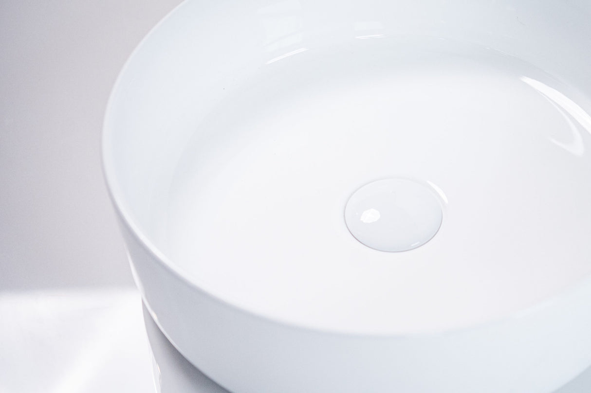 Close-up of a sleek white round ceramic basin with smooth edges and a central drain, showcasing its minimalist and modern design against a soft, neutral background.