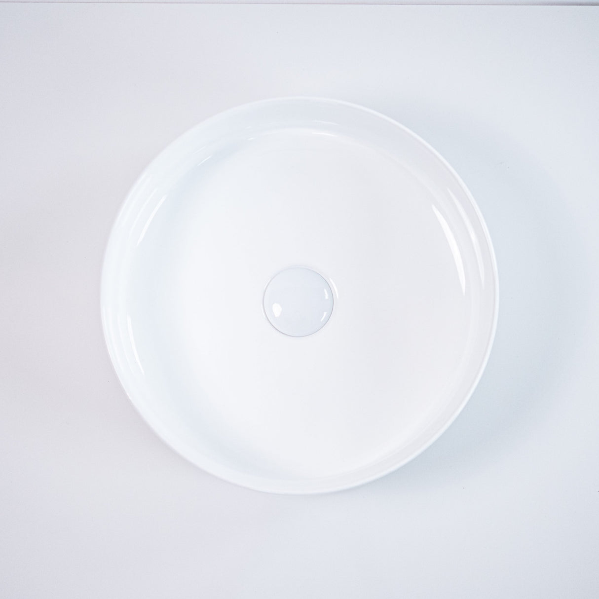 Top-down view of a round white ceramic basin with smooth edges and a central drain, highlighting its minimalist and modern design against a clean white background.