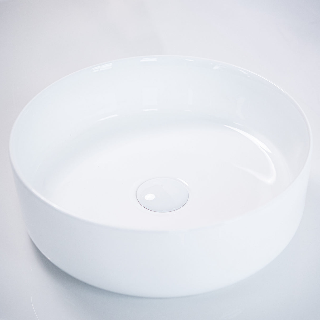 Minimalist white round ceramic basin with smooth edges and a central drain detail, showcased against a clean white background, emphasizing its modern and elegant design.