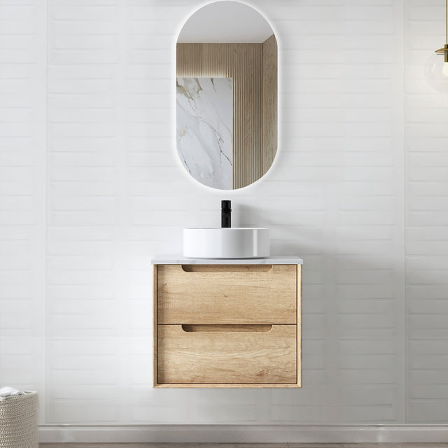 Bathroom vanity with wooden cabinet, white sink, and oval mirror on a light gray wall.