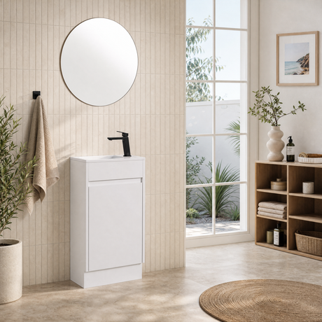 A modern white bathroom vanity cabinet with an integrated sink and matte black faucet, shown in a bright, contemporary bathroom setting with a round mirror, tiled wall, window view, and wooden shelving.