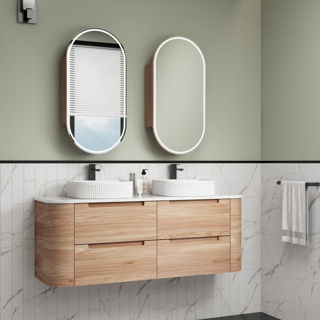 Bathroom vanity with wooden cabinets, white countertop, and two oval mirrors on a green wall.