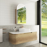 Bathroom with wooden vanity, white sink, and arched mirror reflecting greenery.