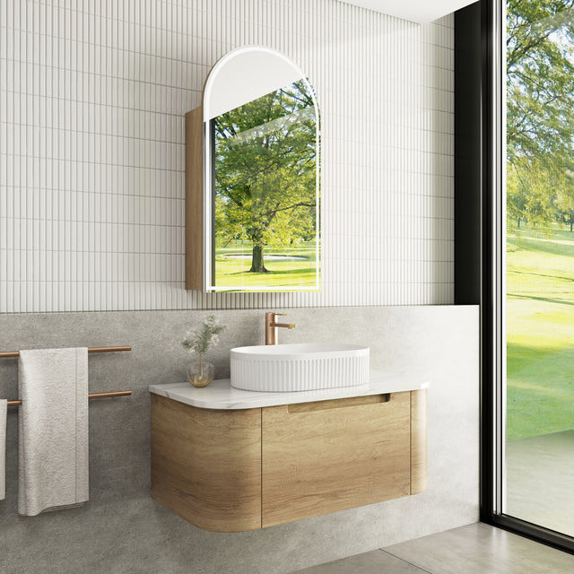 Modern bathroom with wooden vanity, white sink, and large mirror reflecting greenery.