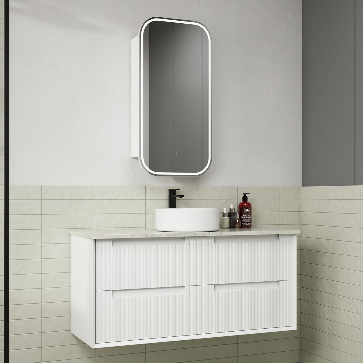 Bathroom vanity with white cabinet, round sink, and mirror above in a tiled bathroom.