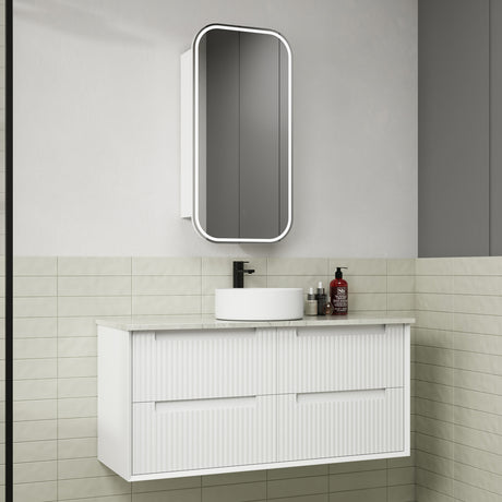Bathroom vanity with white cabinet, round sink, and mirror above in a tiled bathroom.