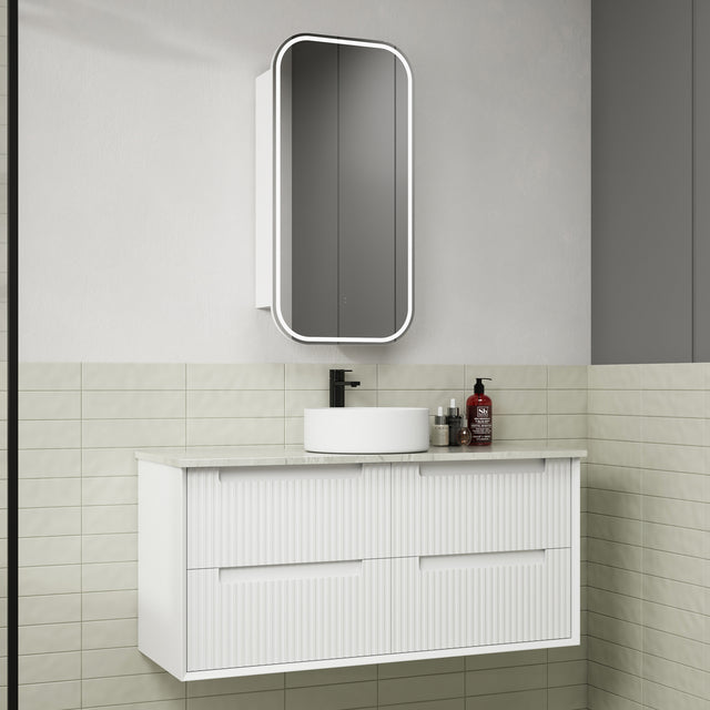 Bathroom vanity with white cabinet, round sink, and mirror above in a tiled bathroom.