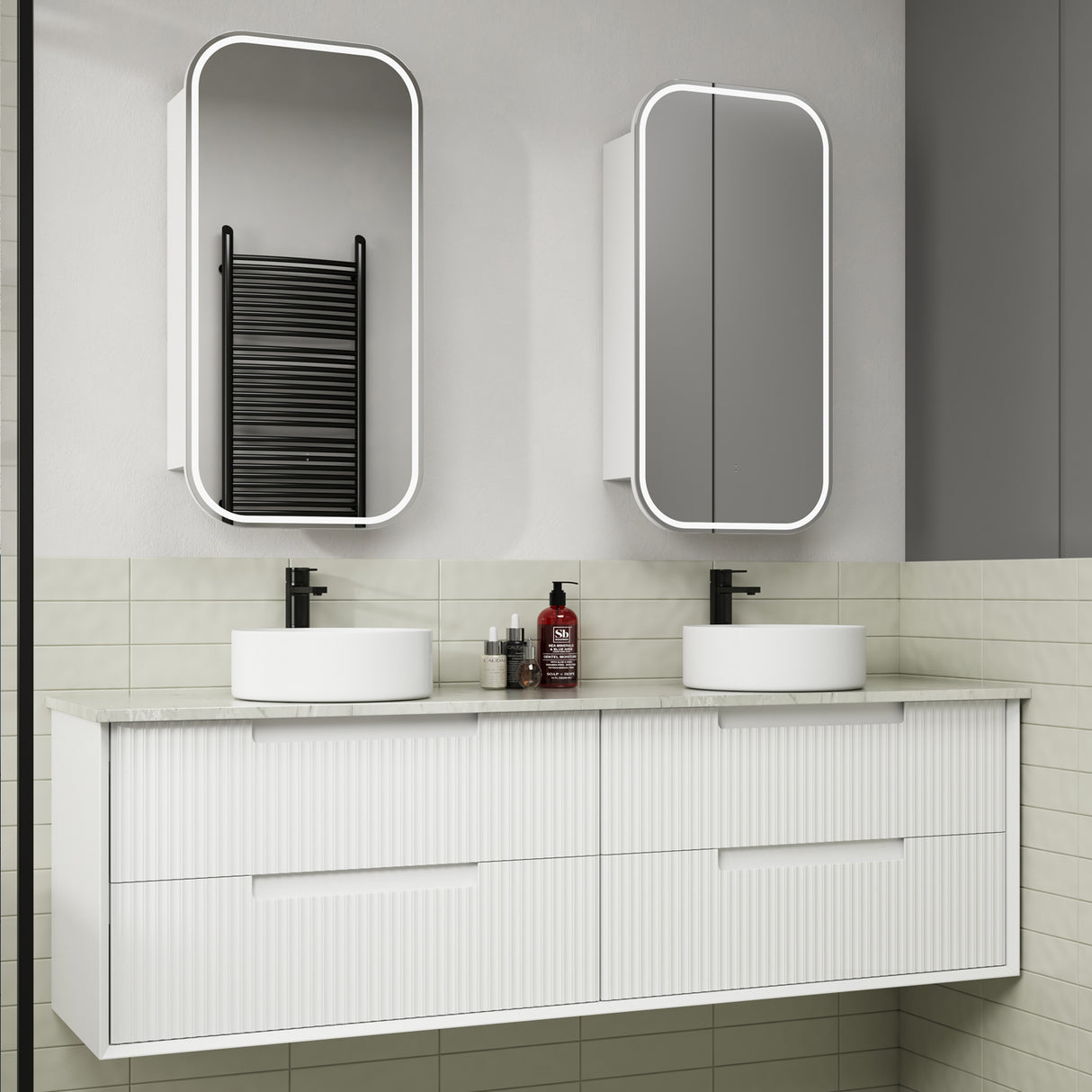 Bathroom vanity with two white sinks, mirrors, and toiletries on a tiled wall.