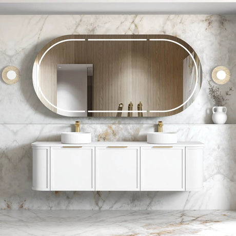 A wall-hung vanity with a curved mirror and brushed gold handles in a white satin finish, with drawers and shelving in a bathroom setting.