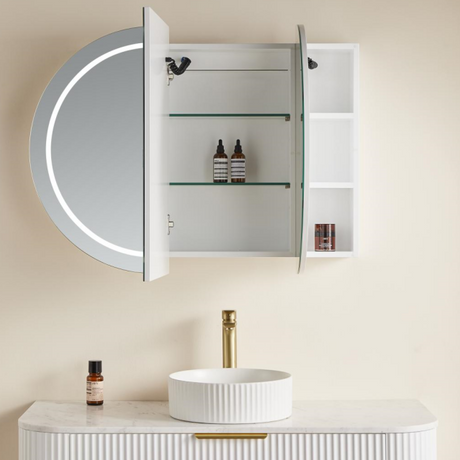 Bathroom setup with round mirror, illuminated cabinet, and sink.