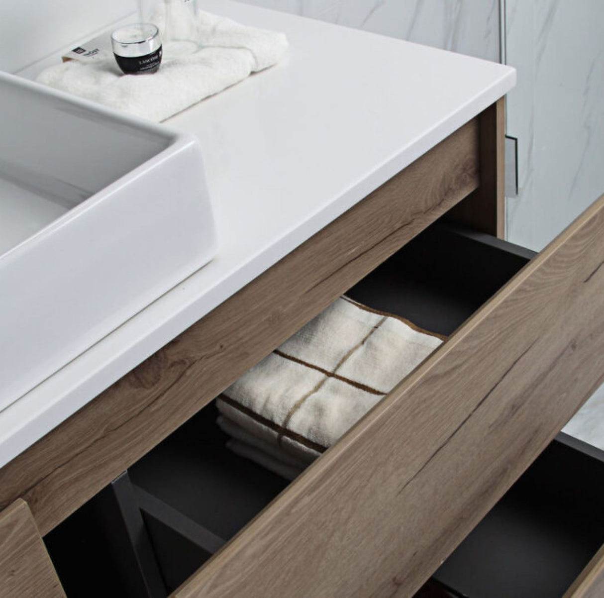 Bathroom vanity with open drawer revealing folded towels, sink, and cup on countertop.