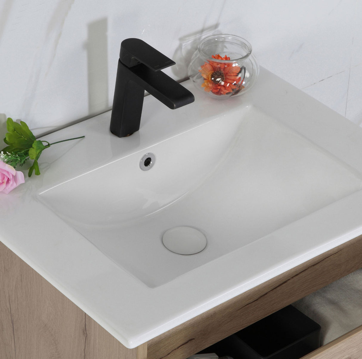 White bathroom sink with black faucet and decorative elements on a light wooden cabinet.