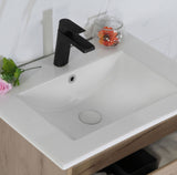 White bathroom sink with black faucet and decorative elements on a light wooden cabinet.