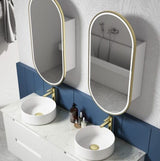 Bathroom vanity with two round white sinks, gold fixtures, and two oval mirrors.