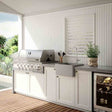 Outdoor kitchen with grill, sink, and refrigerator on a wooden deck.