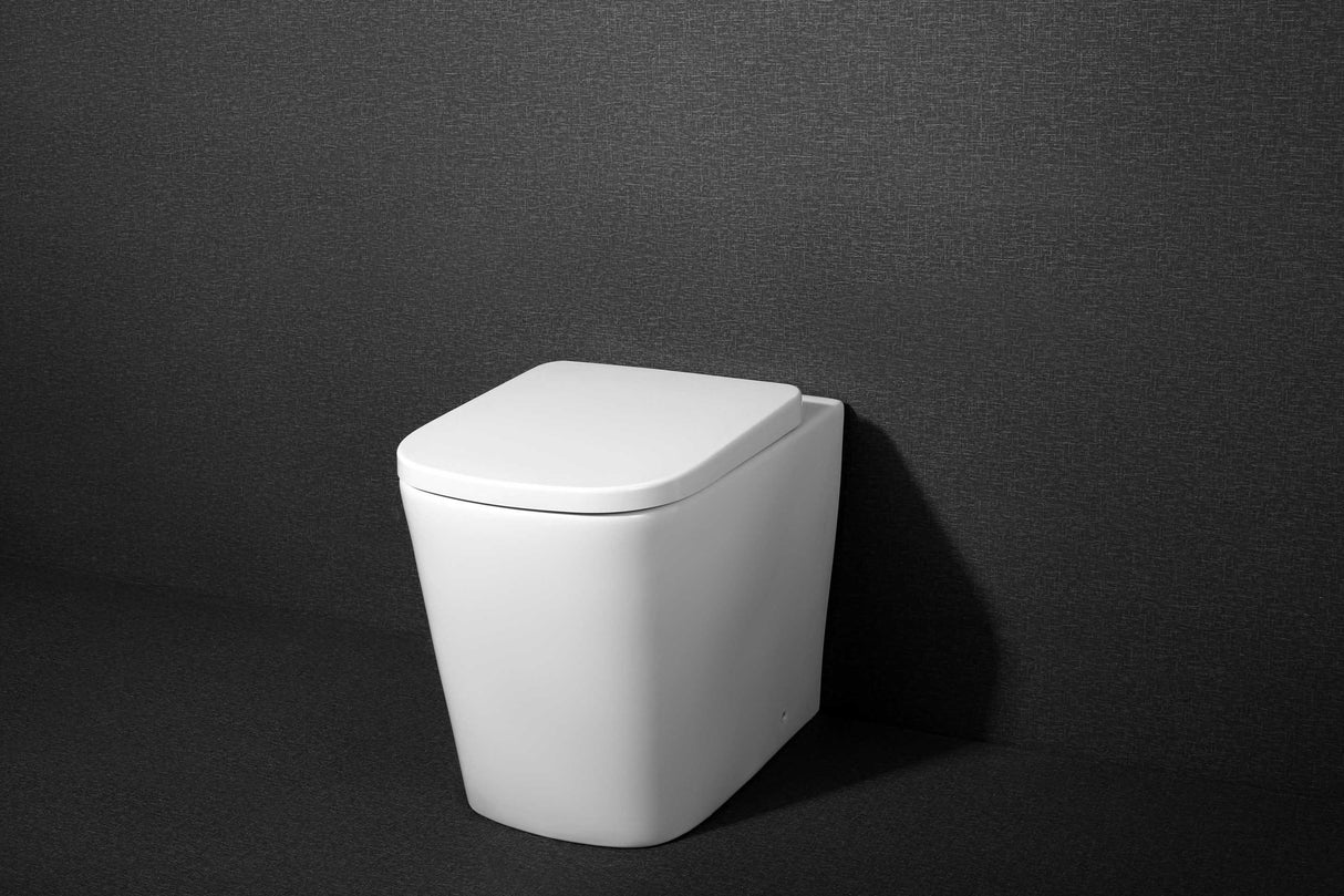 ANITA In Wall Toilet Pan (Square) featuring a sleek, modern white ceramic design, set against a textured dark gray background.