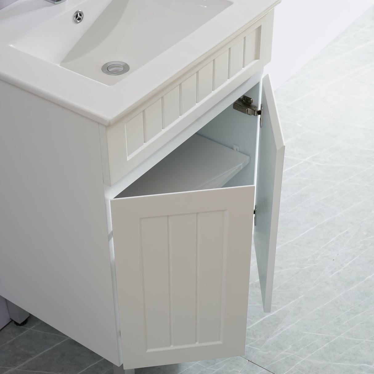 White bathroom vanity with sink and open cabinet door on a tiled floor.
