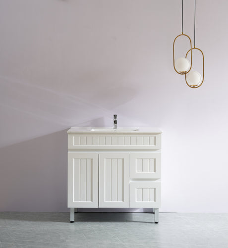 White bathroom vanity with sink against a plain wall with two gold pendant lights.