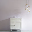 White bathroom vanity with sink against a plain wall with two gold pendant lights.