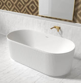 White freestanding bathtub in a bathroom with marble walls and a patterned wall hanging.